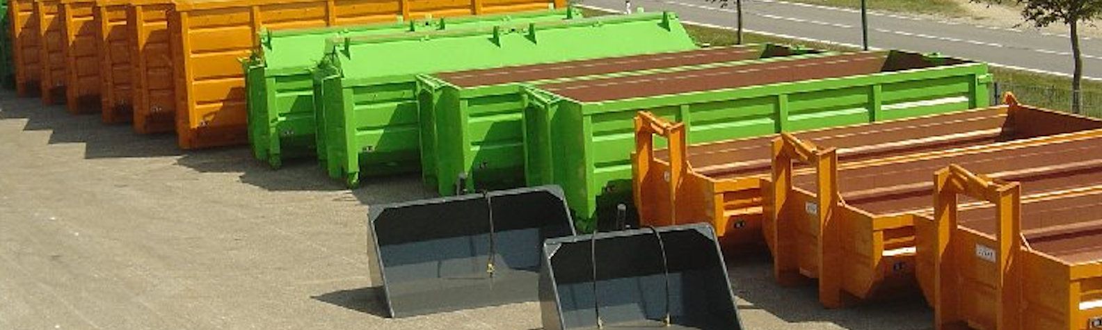 Reihen von orangefarbenen und grünen Absetzcontainern auf einem Hof  Zwei schwarze Ladeschaufeln stehen im Vordergrund